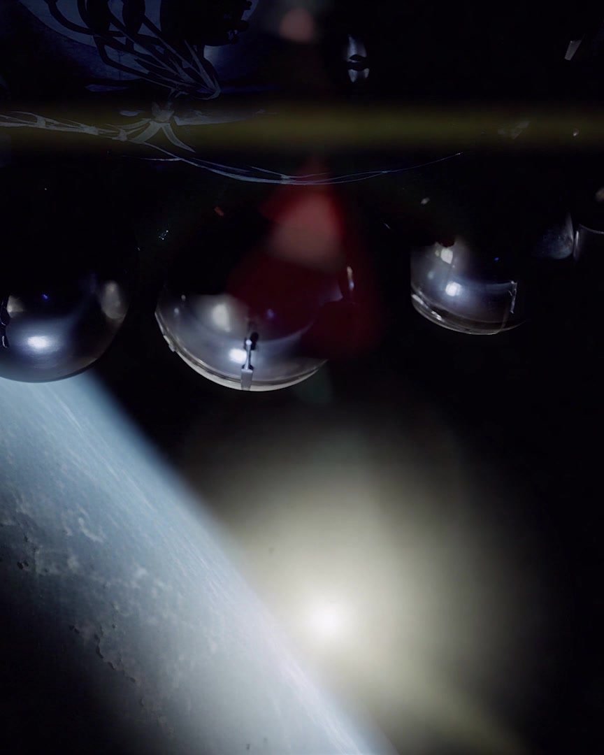 Dark capsule hardware drifting against the curve of the Earth, a lens flare below