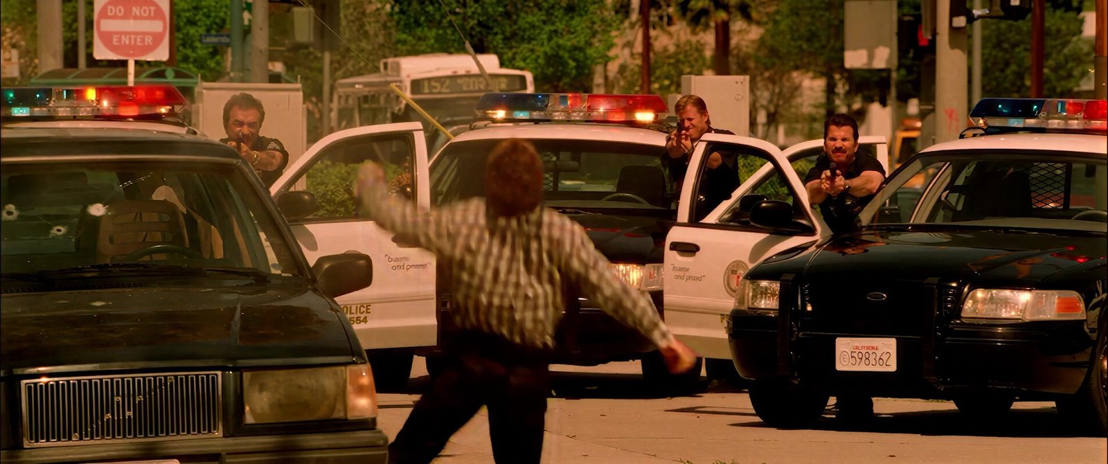A man confronted at gunpoint between squad cars, lights flashing